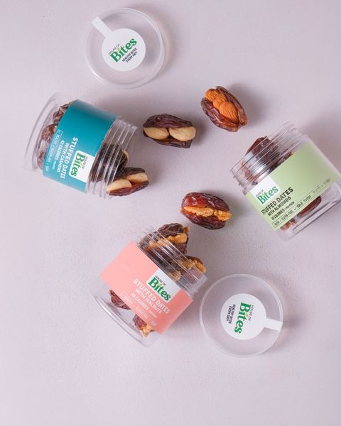 Open stuffed dates jars with cashew, walnut and almond dates spilled on a lilac table.
